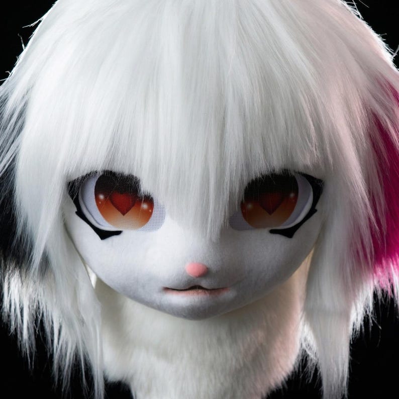 May include: A white furry mask with large, expressive eyes featuring heart-shaped pupils. The mask has long white hair with pink and black accents. The nose is pink, and the mouth is slightly open, creating a cute, cartoonish appearance.