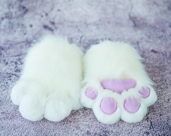 May include: A pair of white furry slippers with pink paw pads. The slippers are soft and fluffy, perfect for keeping your feet warm.
