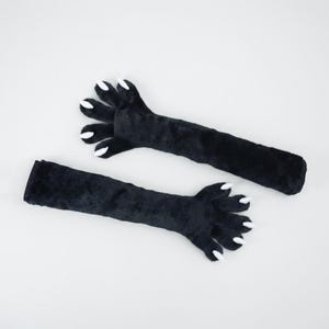 Peut inclure: Deux manchons noirs en peluche en forme de pattes de chat avec des griffes blanches. Les manchons sont longs et ont une texture douce et duveteuse. Les pattes sont détaillées avec des griffes individuelles.