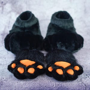 Pu&ograve; includere: Un paio di pupazzi di mano a forma di zampa di orso nero con cuscinetti delle zampe arancioni. I pupazzi sono realizzati in tessuto morbido e peluche e hanno un aspetto realistico.