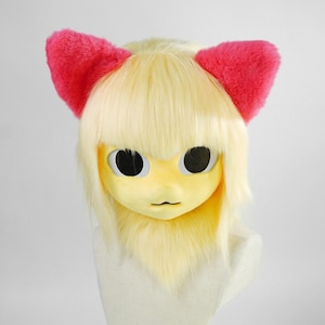 May include: A full-head mask featuring pale yellow synthetic fur and hair with straight bangs. The mask has large, round, black eyes and a small mouth. Two bright pink, fuzzy, triangular ears are attached to the top of the head.