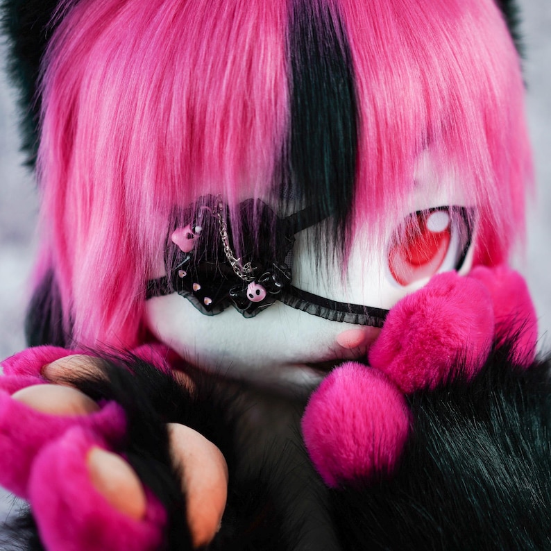May include: A pink and black furry creature with a black eye patch and pink paws. The creature has a pink and black striped hairstyle.