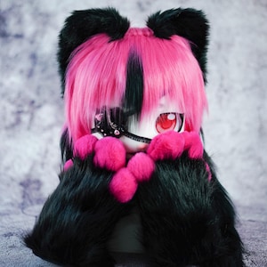 May include: A plush toy with black fur and pink ears, wearing a pink and black wig with a black eye patch. The toy has a white face with red eyes and is holding its paws in front of its face.