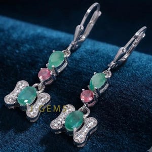 May include: A pair of silver-toned drop earrings featuring a lever-back closure. Each earring displays a vertical arrangement of a pear-shaped green gemstone, a round pink gemstone, and an oval green gemstone set within a butterfly-shaped base.