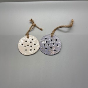 May include: Two ceramic ornaments with a hole pattern. One is white and the other is a light purple with gold flecks.