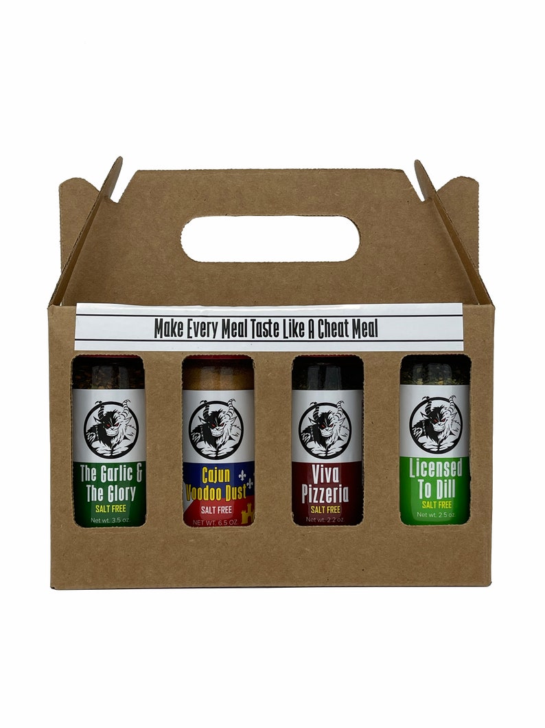 May include: A cardboard box with a handle contains four small glass bottles of salt-free seasoning blends. The bottles are labelled "The Garlic & The Glory", "Cajun + Voodoo Dust", "Viva Pizzeria", and "Licensed To Dill".