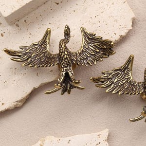 Puede incluir: Dos tiradores de armario antiguos con forma de pájaro de latón con alas extendidas. La ferretería decorativa presenta plumas detalladas y un acabado vintage. Estos tiradores son ideales para añadir un toque de elegancia a los muebles.