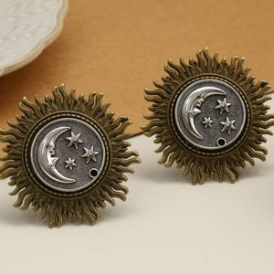Peut inclure: Deux boutons de meuble en bronze antique. Chaque bouton présente un motif de soleil autour d'un centre circulaire avec un croissant de lune et trois étoiles. Les boutons sont probablement destinés aux meubles ou à la décoration.