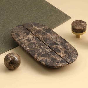 May include: A set of dark brown marble hardware including one spherical knob, one elongated oval handle split into two pieces, and two cylindrical knobs with gold-toned metal bases. The marble features a natural veined pattern throughout.