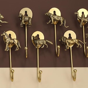 Peut inclure: Ensemble de huit crochets muraux en laiton ornés d'animaux. Chaque crochet représente un animal différent : taureau, ours, tigre, chameau, cheval, loup, lion et girafe. Montés sur un mur marron et beige.
