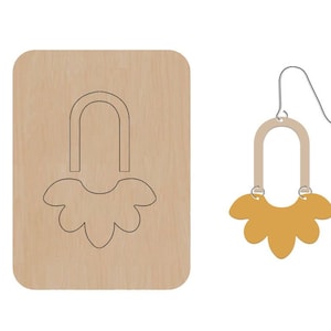 Puede incluir: Una plantilla de madera para hacer un par de pendientes. La plantilla muestra un pendiente con forma de flor con la parte superior curvada.