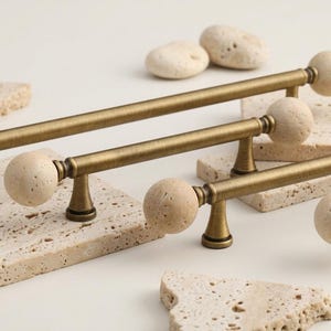 May include: Antique brass cabinet pulls with spherical stone accents. The pulls have a cylindrical bar and are mounted on a decorative stone surface. The hardware is designed for furniture and home decor.