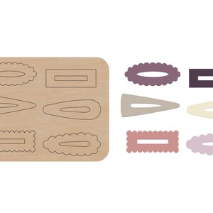 May include: A wooden sheet with eight different hair clip templates. The templates are in various shapes and sizes, including oval, rectangular, and teardrop shapes. The templates are outlined in black and ready to be cut out.