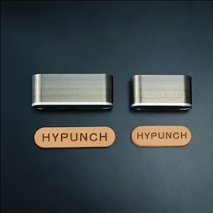 May include: Two silver metal oval-shaped leather punches with the word "HYPUNCH" embossed on two brown leather samples.