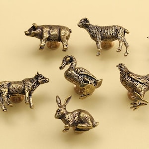 Puede incluir: Un conjunto de tiradores de armario de animales de latón antiguo, que incluyen un cerdo, una oveja, un pato, una vaca, un conejo y una gallina. Estos tiradores decorativos añaden encanto rústico.