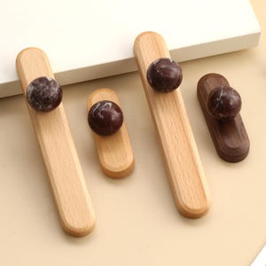 May include: A collection of wooden cabinet pulls with a dark, speckled sphere accent. The pulls are in various shapes and wood tones, including light and dark brown. These decorative knobs are ideal for furniture upgrades.
