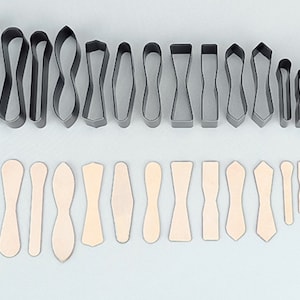 Może przedstawiać: Zestaw 16 metalowych foremek do ciasteczek w różnych kształtach, w tym muszki, serca i owale. Formy są ułożone w dwóch rzędach, z większymi formami w górnym rzędzie i mniejszymi formami w dolnym rzędzie. Formy są wykonane z błyszczącego, srebrnego metalu.