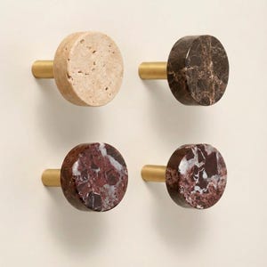 May include: Four decorative cabinet knobs with brass stems. The knobs are made of natural stone in various colors: beige, dark brown, and red with white veining. The knobs are round and have a smooth, polished finish.