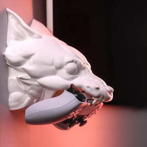 Może przedstawiać: Biała ceramiczna głowa wilka mocowana do ściany z białym kontrolerem do gier wideo w pysku.