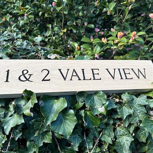 May include: A wooden sign with the text "1 & 2 VALE VIEW" engraved in black lettering.