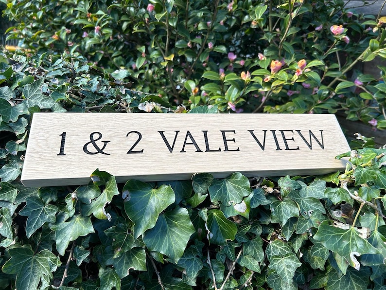 May include: A wooden sign with the text "1 & 2 VALE VIEW" engraved in black lettering.