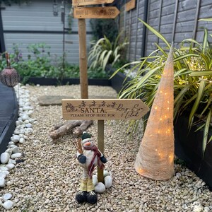 May include: A wooden sign with the text "Please stop here for Santa" and a snowman figurine standing on a bed of gravel.