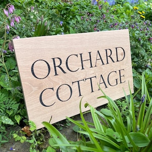 May include: A wooden sign with the text "Orchard Cottage" in black lettering.