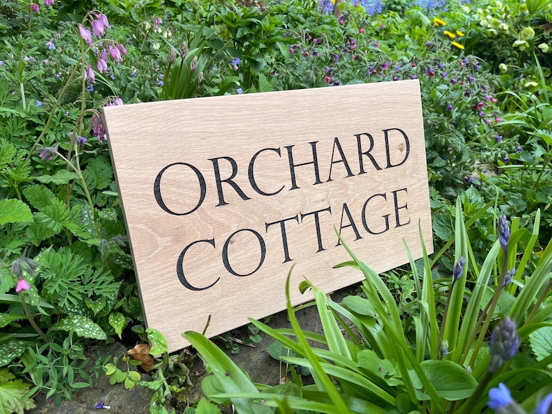 May include: A wooden sign with the text "Orchard Cottage" in black lettering.