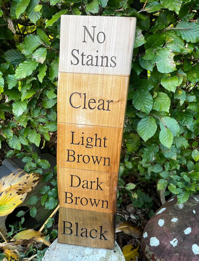 May include: A wooden sign with five sections, each stained a different color. The sections are labeled "No Stains", "Clear", "Light Brown", "Dark Brown", and "Black".