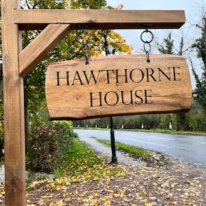 May include: A wooden sign with the text "HAWTHORNE HOUSE" hanging from a wooden post. The sign is brown and has a natural wood finish. The post is also brown and has a natural wood finish. The sign is hanging from two black chains.