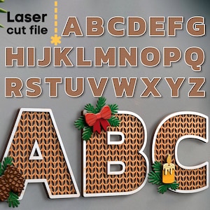 Op de afbeelding: Lasergesneden bestand van het alfabet in hoofdletters. De letters zijn bruin met een witte omtrek en hebben een gebreide textuur. De letters A, B en C worden in een grotere maat weergegeven met decoratieve elementen.
