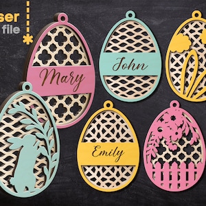 Puede incluir: Seis adornos de huevos de Pascua de madera cortados con láser con diferentes diseños. Los huevos están pintados en varios colores, incluyendo rosa, amarillo, azul y verde. Los diseños incluyen un conejito, flores y un patrón geométrico. Los huevos tienen nombres escritos en ellos, incluyendo Mary, John y Emily.
