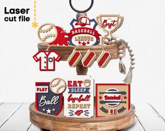 May include: Laser cut wooden baseball themed decorations. The decorations include a baseball jersey, a baseball with stars, a trophy with the text "the best", a sign that says "Baseball League", three hot dogs, a sign that says "Play Ball", a sign that says "Eat Sleep Baseball Repeat", and a sign that says "Baseball #1".