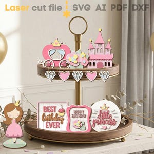 Puede incluir: Un soporte de madera de dos niveles con decoraciones temáticas de princesas. El nivel superior presenta un carruaje y un castillo rosas. El nivel inferior tiene una figura de princesa y letreros que dicen "Best birthday ever", "Happy Birthday" y "Little Princess".
