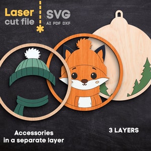 May include: A three-layer laser cut file design featuring a fox wearing a hat and scarf. The components include a circular frame, a fox face, and a back panel with pine trees. Text includes Laser cut file, SVG, AI, PDF, DXF, Accessories in a separate layer, and 3 LAYERS.