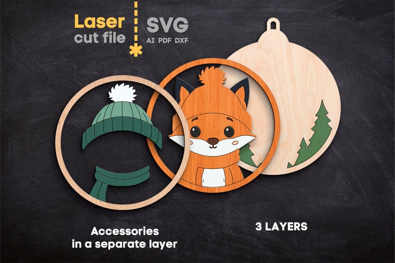 May include: A three-layer laser cut file design featuring a fox wearing a hat and scarf. The components include a circular frame, a fox face, and a back panel with pine trees. Text includes Laser cut file, SVG, AI, PDF, DXF, Accessories in a separate layer, and 3 LAYERS.