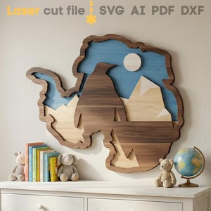 May include: A wooden wall art piece in the shape of Antarctica, featuring a penguin, mountains, and a moon against a blue sky. The artwork is made of layered wood in shades of brown, beige, and blue. The text "Laser cut file SVG AI PDF DXF" is at the top.