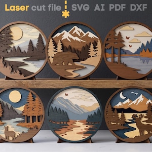 Puede incluir: Seis obras de arte murales redondas de madera con diseños de paisajes en capas. Cada pieza presenta una escena natural diferente, incluyendo montañas, bosques, ríos y fauna. El texto "Laser cut file" es visible en la parte superior.