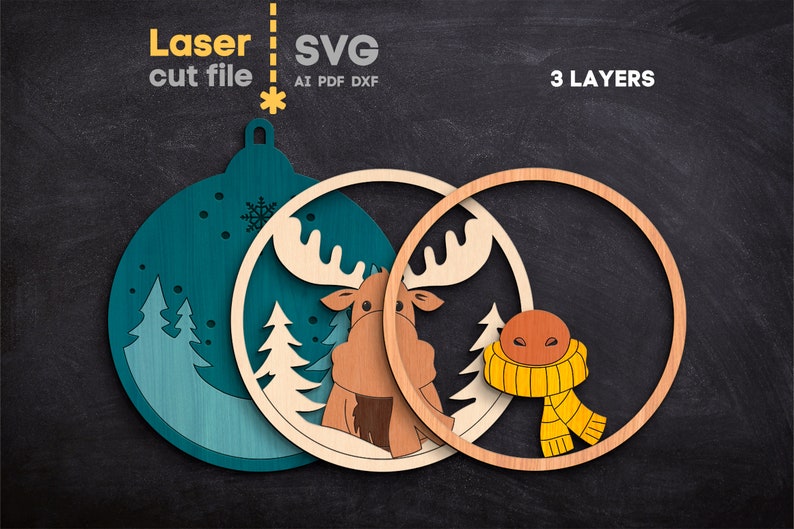 May include: A three-layer laser cut file for a Christmas ornament featuring a teal background with pine trees and snowflakes, a light wood layer with a moose, and a wood ring layer with a brown moose nose and a yellow scarf. Text reads Laser cut file SVG AI PDF DXF 3 LAYERS.