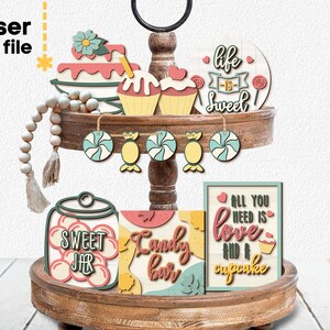 May include: A tiered wooden tray decorated with laser cut wood shapes. The shapes include cupcakes, candy, a jar labeled "Sweet Jar", and signs that say "Life is Sweet" and "All you need is love and a cupcake".