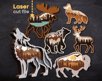 May include: Wooden laser cut file featuring six different wildlife animal designs: a moose, a wolf, a bear, a deer, a fox, and a bison. Each animal has a layered design with a mountain and forest scene inside. The text "Laser cut file" is in the upper left corner.