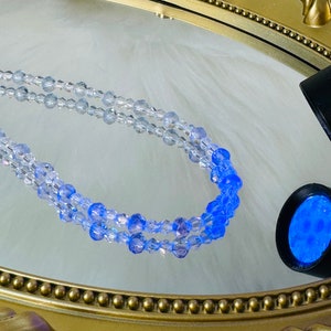 May include: A double strand of light blue and clear glass beads on a gold tray.
