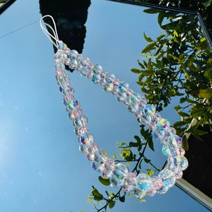 以下が含まれることがあります： 白い紐の付いた、透明な虹色のクリスタル製の携帯電話チャーム。チャームは複数の丸いビーズでできています。