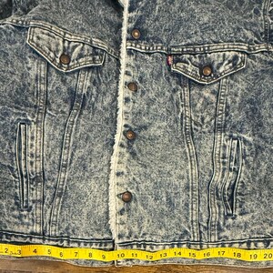 Puede incluir: Chaqueta vaquera con lavado &aacute;cido y forro de borreguillo color crema. La chaqueta tiene dos bolsillos en el pecho y dos bolsillos laterales. La chaqueta est&aacute; abotonada y tiene una cinta m&eacute;trica amarilla en la parte inferior. La chaqueta mide unos 53 cm en la parte inferior.