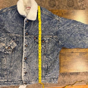 Puede incluir: Chaqueta vaquera con cuello y forro de borreguillo blanco. La chaqueta tiene un patr&oacute;n de lavado &aacute;cido azul, cierres de bot&oacute;n y dos bolsillos en el pecho. La longitud de la chaqueta es de aproximadamente 63,5 cm.