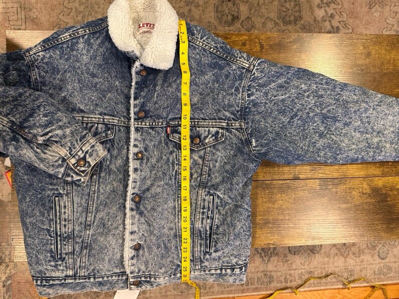 Puede incluir: Chaqueta vaquera con cuello y forro de borreguillo blanco. La chaqueta tiene un patr&oacute;n de lavado &aacute;cido azul, cierres de bot&oacute;n y dos bolsillos en el pecho. La longitud de la chaqueta es de aproximadamente 63,5 cm.