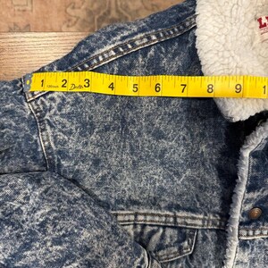 Puede incluir: Chaqueta vaquera con cuello de borreguillo blanco. La chaqueta est&aacute; lavada a la piedra y tiene una cinta m&eacute;trica amarilla sobre el hombro, que muestra una medida de aproximadamente 23 cm.