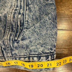 Puede incluir: Primer plano de una chaqueta vaquera azul con un ligero lavado &aacute;cido. Una cinta m&eacute;trica amarilla muestra una longitud de aproximadamente 40 a 61 cm. La chaqueta tiene bolsillos y costuras.