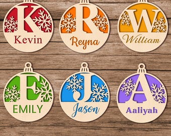 May include: Circular wooden Christmas decorations with individual names and initials. Each bauble has a different coloured background: red, orange, yellow, green, blue, and purple. Snowflake designs and the names Kevin, Reyna, William, Emily, Jason, and Aaliyah are visible.
