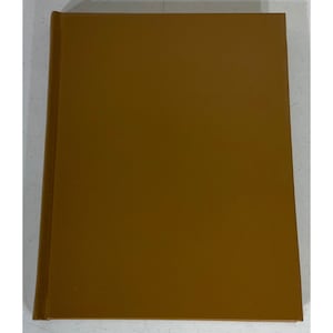 May include: A rectangular hardcover book with a solid, plain mustard-yellow cover. The book is positioned vertically, showing the front cover and the spine edge on the left side. The surface of the cover appears smooth and uniform in color.